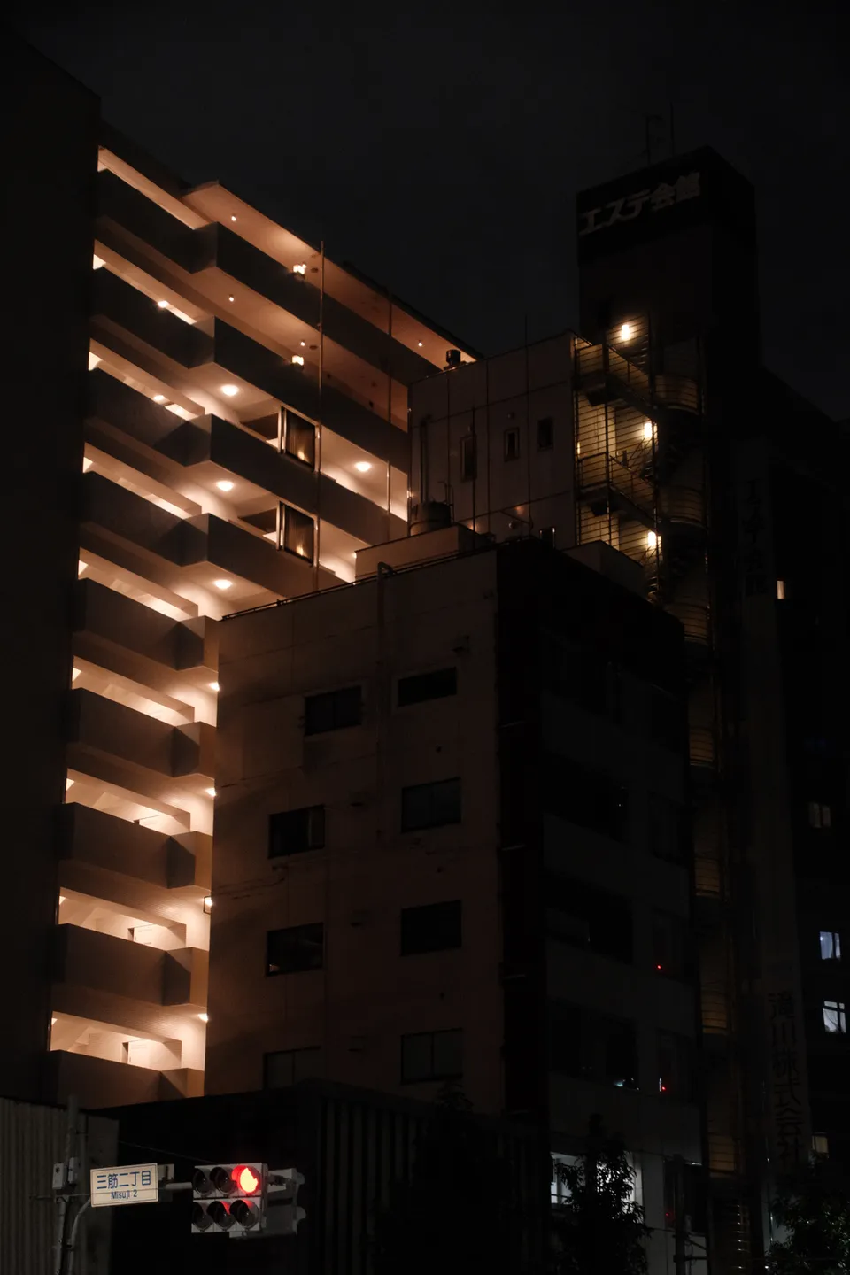 Ein mehrstöckiges Gebäude mit beleuchteten Balkonen neben einem dunkleren Wohnblock bei Nacht.