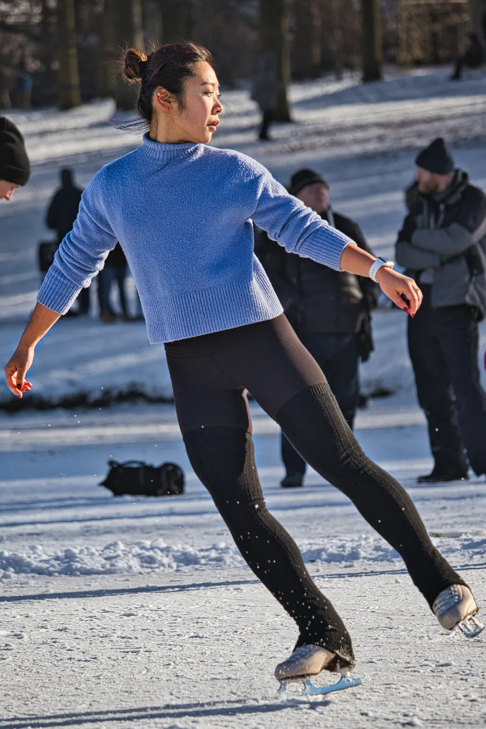 Eine Person in einem blauen Pullover und dunklen Leggings läuft auf einer Eisfläche.