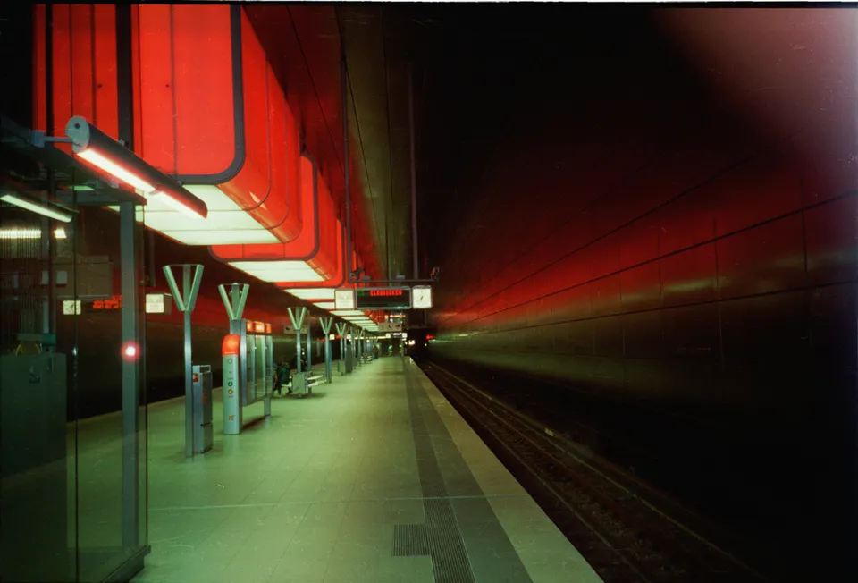 Eine moderne U-Bahnstation mit leuchtend roten Deckenelementen und einem langen Bahnsteig.
