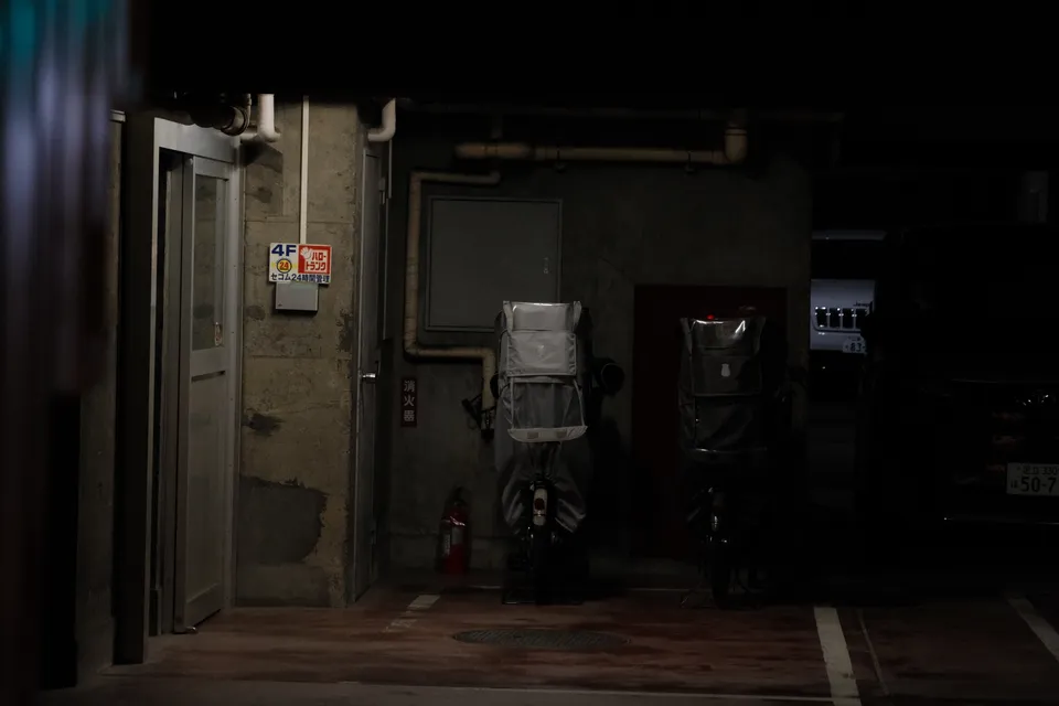 Zwei mit Kisten bestückte Motorroller stehen vor einem Gebäude bei Nacht.