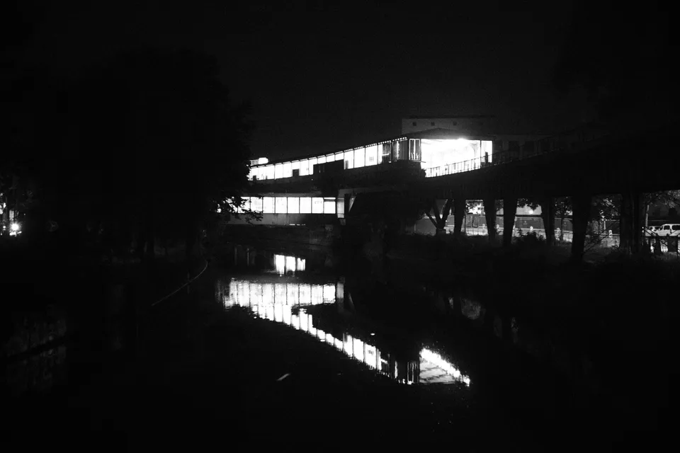Eine hell erleuchtete Brücke spiegelt sich in einem dunklen Gewässer bei Nacht.
