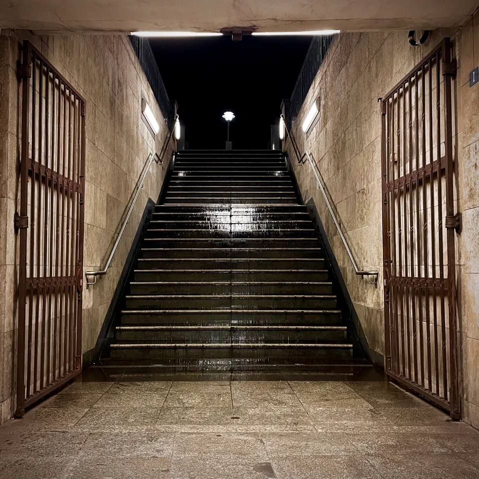 Eine beleuchtete Steintreppe führt nach oben zwischen zwei großen Metalltoren in der Nacht.